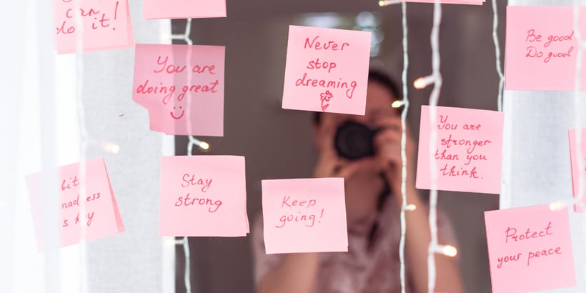 An image illustrating the meaning of what are affirmations, with a person holding a note card that reads 'I am worthy' surrounded by positive affirmations written on a whiteboard.